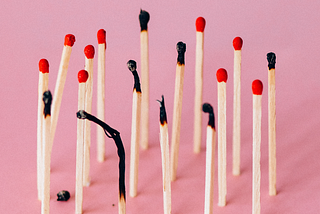 A pink background with standing matches. Some are burned and bent representing burnout.