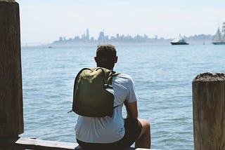 A man sitting on a bench wearing the MTW Backpack looking at San Francisco.