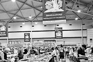 A black and white photo of Brisbane Lifeline Bookfest featuring long tables of books for sale and shoppers browsing.