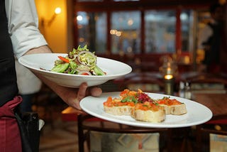 A waiter balancing two plates, one with a salad and the other with bruschetta.