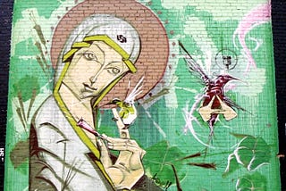 Mural on a brick wall of a smiling Madonna with a hummingbird perched on her finger