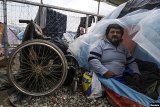 A person with physical disability siting beside his tent in a refugee camp, with his wheel chair by the side