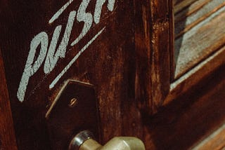 A wooden door with brass pull handle and the words ‘PUSH’ painted above.