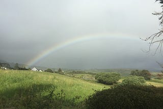 A rainbow arches over green fields and hills.