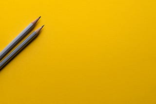 Two pencils on a yellow surface.