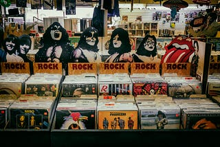 Rock album bins at used vinyl record store. Images of members of KISS and the Rolling Stones’ “mouth and extended tongue” logo displayed above.