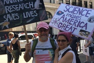 Man and woman with pink hats holding signs.