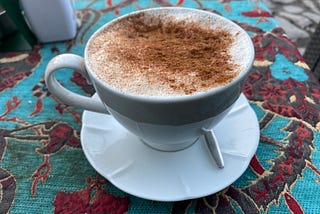 A cup sits on a saucer, the drink covered in cinnamon.