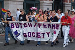 A group of butch and femme lesbians carrying a banner that says Butch/Femme Society at the New York gay pride parade