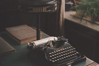 A dimly lit room with an old typewriter on the desk and plants on a faraway table