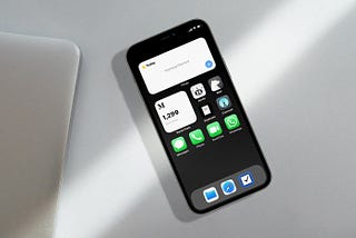 An iPhone 12 Mini sitting on top of a desk with a MacBook on its left