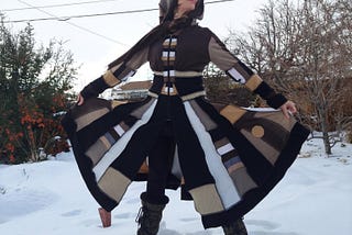A woman in a sweater coat of brown, white and black, posing in a snowy backyard setting.
