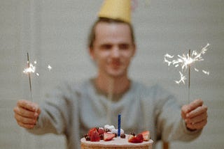 A man with a birthday hat, cake, and lights. It shows the appreciation of life, living the day and moment happily.