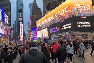 A crowded Times Square in New York, with a digital billboard that reads, “WELCOME BACK NYC”