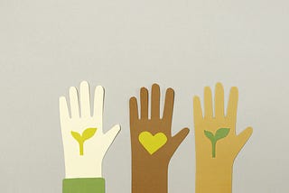 Paper cutouts of three hands in different skin tones with plants and a heart in the palms.