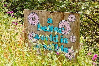 Hand painted plywood sign with donuts and the phrase, “a better world is possible”