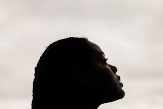 A Black woman looks up pensively in a white background.