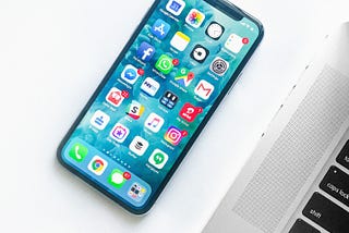Iphone with many apps next to a laptop