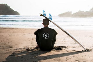 A man sitting at the beach looking at the sea, the sun is setting