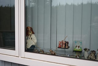 写真。恥ずかしそうに窓枠の陰から外を覗く動物の人形たち。