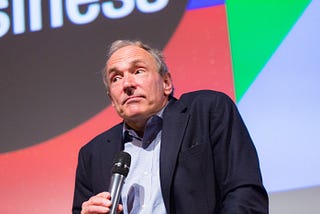 Tim Berners-Lee holding a microphone and shrugging
