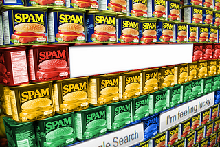 A wall of Spam cans stacked many layers high and deep. Superimposed over it are UI elements from the Google 1998 homepage: a search box, a ‘Google Search’ button, and an ‘I’m feeling lucky’ button. The middle four rows of Spam cans have been colorized to match the Google four-color logo tones. Image: freezelight (modified) https://commons.wikimedia.org/wiki/File:Spam_wall_-_Flickr_-_freezelight.jpg CC BY-SA 2.0 https://creativecommons.org/licenses/by-sa/2.0/deed.en