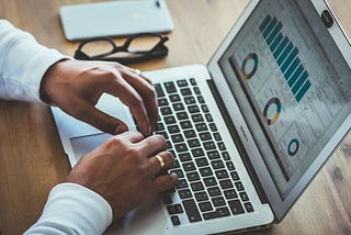 Hands typing on laptop displaying various charts