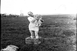 Black and white photo of man bathing while standing in a crate