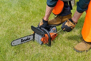 A man bending over to pick up a chainsaw.