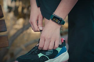 Person adjusting their running shoes while wearing a fitness tracker