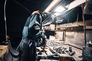 A skilled craftsman in protective welding gear meticulously works on vacuum castings at Uni Tritech’s manufacturing facility, demonstrating the company’s commitment to quality and precision in metal fabrication