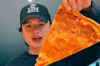 Student holding slice of pizza that he was sent in the mail by Colgate University.