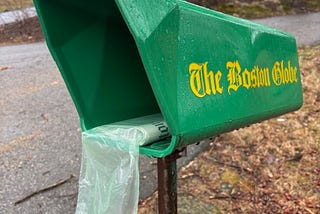 A Boston Globe newspaper tube with a plastic wrapped newspsper in it.