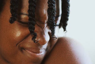 Photo of a young black woman with braids, grimacing with her eyes closed.