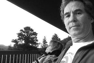 Black and white photo of author and spouse sharing moment of contentment on front porch of cabin.