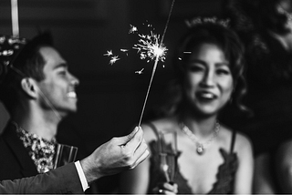 Two friends smiling, holding out lit sparklers to show how excited they are to celebrate the new year.