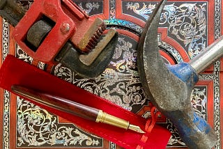 A wrench, a hammer and a fancy pen lying on an expensive notebook