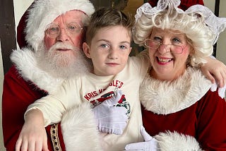 An 8 year old boy nestled between Santa and Mrs. Claus