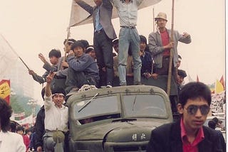 Some Chinese workers atop a truck holding up the sign “工人来了！” (“The workers are here!”) during the 1989 Tiananmen protests.