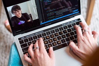 Person typing code on a laptop while on a video call with another person