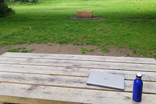 A closed laptop and a water bottle on a picnic bench in a park
