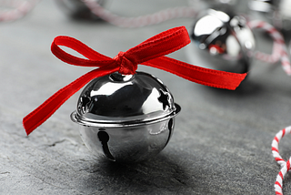 A silver sleigh bell with a red ribbon on a grey table