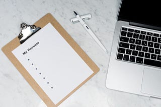 A clipboard, an open pen and an open laptop placed on a table