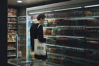 A man stands in front of a refrigerated grocery display, examining items carefully as he decides what to buy.