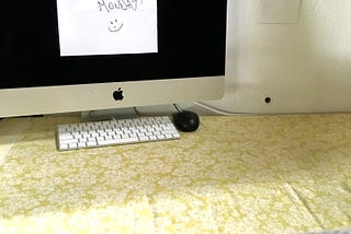 A desk with a computer monitor that has a note attached to it “Office closed until Monday”