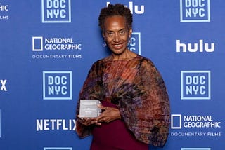 Marcia Smith posing with her Lifetime Achievement Award against a blue-branded DOC NYC step-and-repeat.