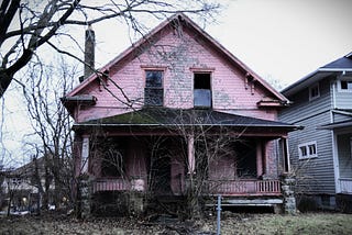 A worn suburban house with peeling paint and a sagging porch.