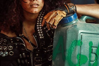 A woman in ‘apocalype gear’, looking rugged and scrappy, holding a large water container