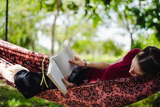 the image shows a young woman lying in a hammock reading a book