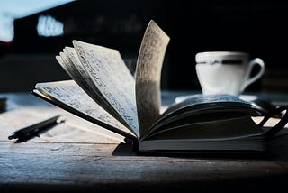 Journal flipping through the pages with a cup of coffee and a pen to the right. Photo by <a href=”https://unsplash.com/@yanu?utm_source=unsplash&utm_medium=referral&utm_content=creditCopyText">Yannick Pulver</a> on <a href=”https://unsplash.com/photos/hopX_jpVtRM?utm_source=unsplash&utm_medium=referral&utm_content=creditCopyText">Unsplash</a>